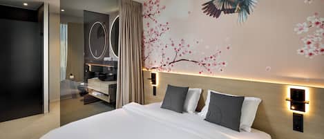 A modern hotel room with a large bed, a vanity with a mirror, and a wall mural of a bird and cherry blossoms.