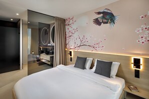 Ett modernt hotellrum med en stor säng, en sminkbord med spegel och en väggmålning som föreställer en fågel och körsbärsblommor.