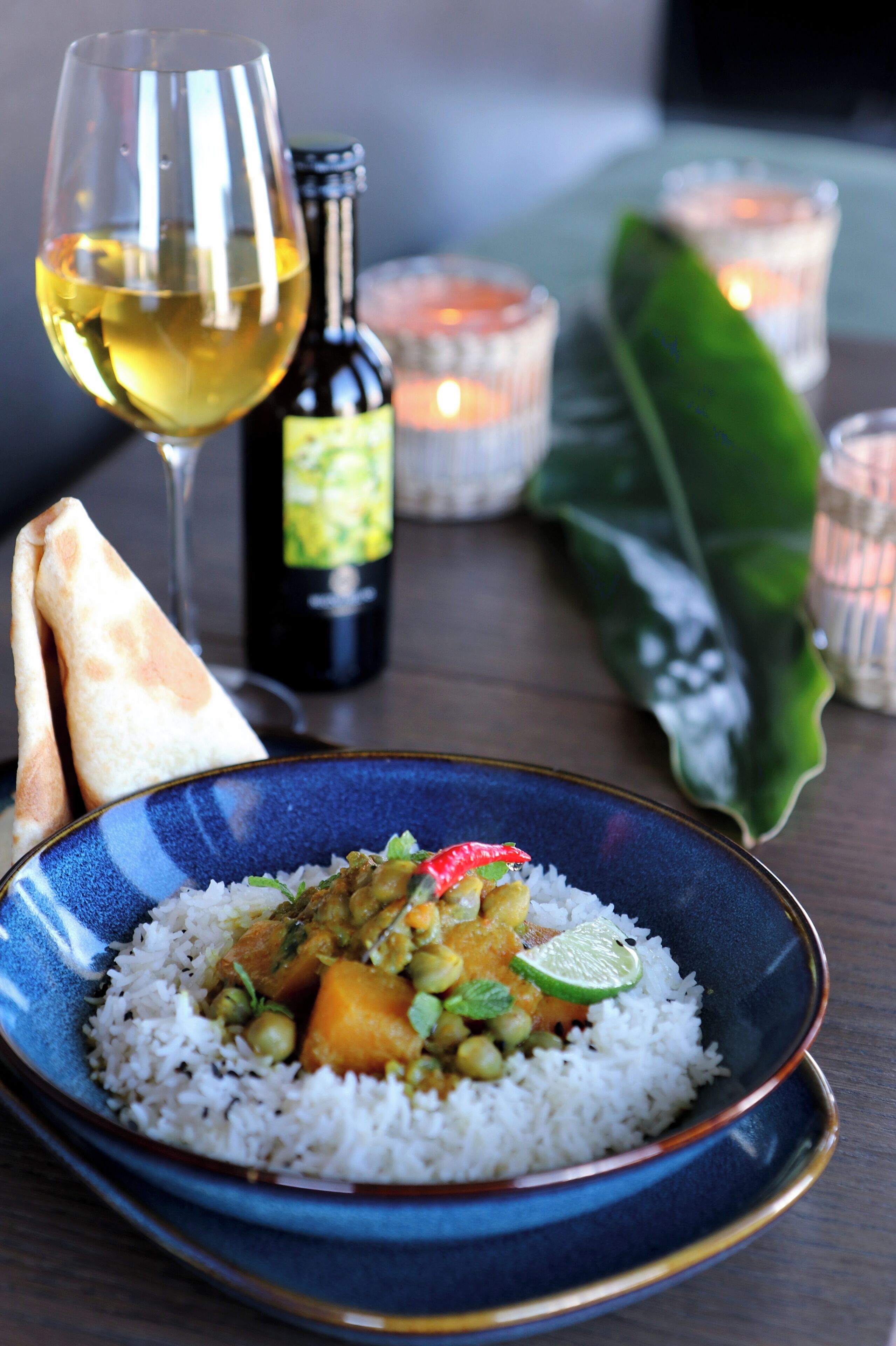 Un bol de riz aux légumes et un verre de vin blanc sur une table éclairée à la bougie, avec une bouteille de vin à proximité.