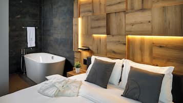 A modern hotel room with a large bed, a bathtub, and a wooden headboard with integrated lighting.