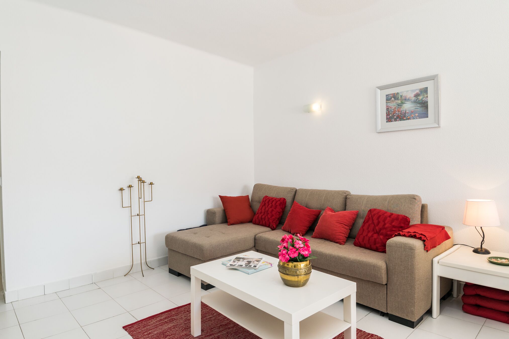 A modern living room with a beige sofa, red cushions, a white coffee table, and a red rug.