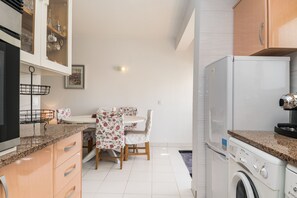 A compact kitchen with a washing machine, a dining area with floral tablecloths, and a built-in cabinet with glass doors.