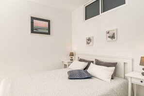 A neatly arranged bedroom with a bed, two bedside tables, a nightstand, and wall-mounted artwork.
