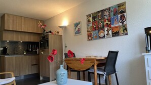 A modern kitchen with wooden cabinets, a dining table with chairs, and a vase with red flowers on a small table. - Cozy Studio with Balcony near Ski Slopes and Town Center - Sleeps 4 (Villard-de-Lans)