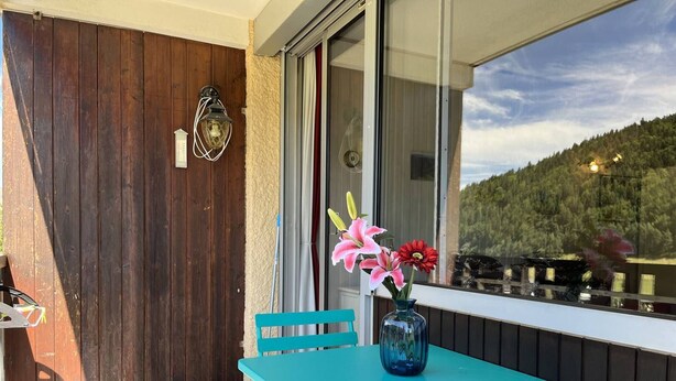 A balcony with a turquoise table and chairs, a vase with flowers, and a view of a forested area. - Cozy Studio with Balcony near Ski Slopes and Town Center - Sleeps 4 (Villard-de-Lans)