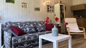 A living room with a patterned sofa, a white table, a vase with red flowers, and a kitchen area in the background. - Cozy Studio with Balcony near Ski Slopes and Town Center - Sleeps 4 (Villard-de-Lans)