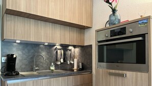 A modern kitchen with wooden cabinets, stainless steel appliances, and a built-in oven. - Cozy Studio with Balcony near Ski Slopes and Town Center - Sleeps 4 (Villard-de-Lans)