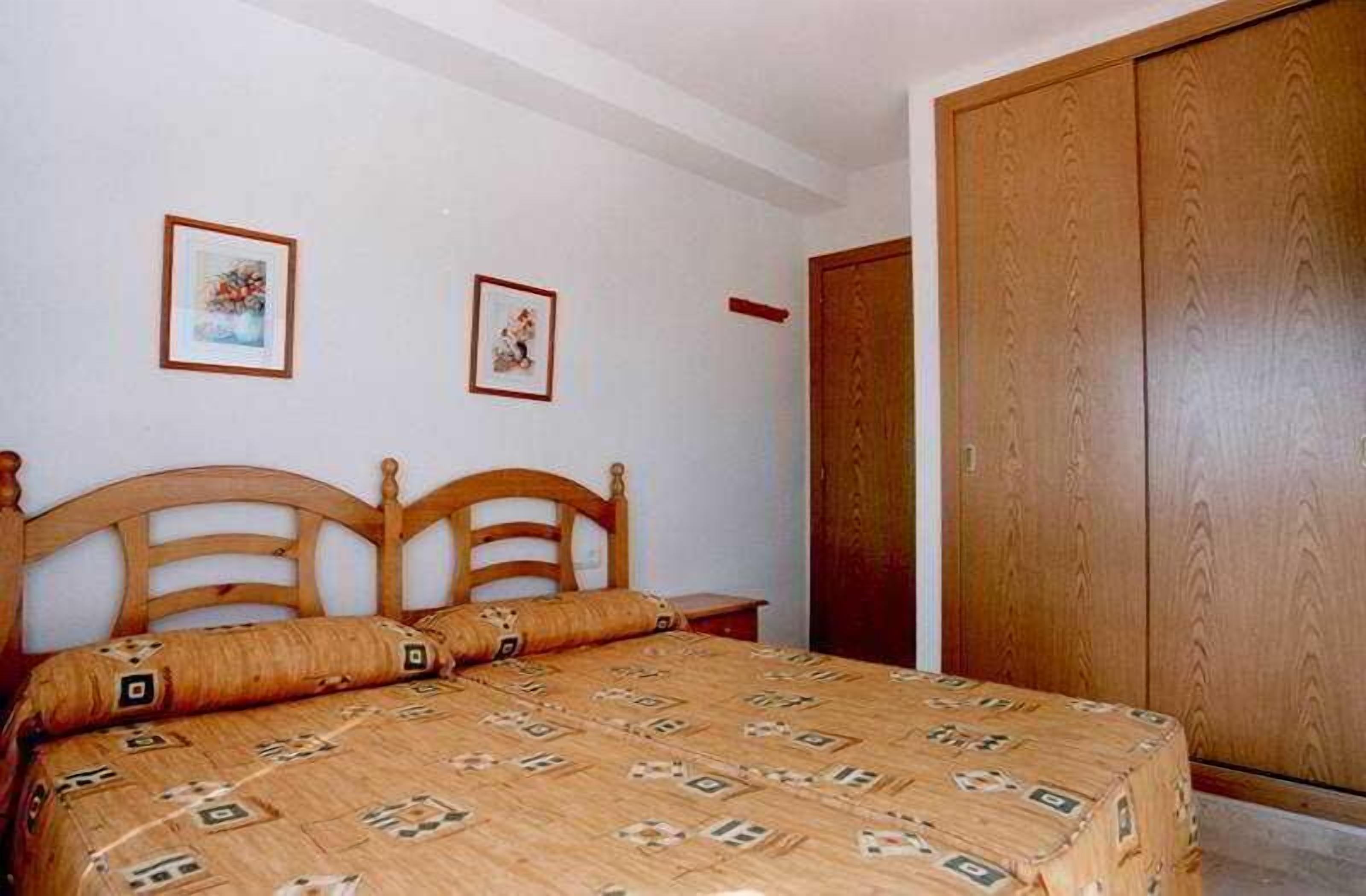 Une chambre à coucher avec un lit en bois, deux tableaux encadrés accrochés au mur et une armoire en bois.