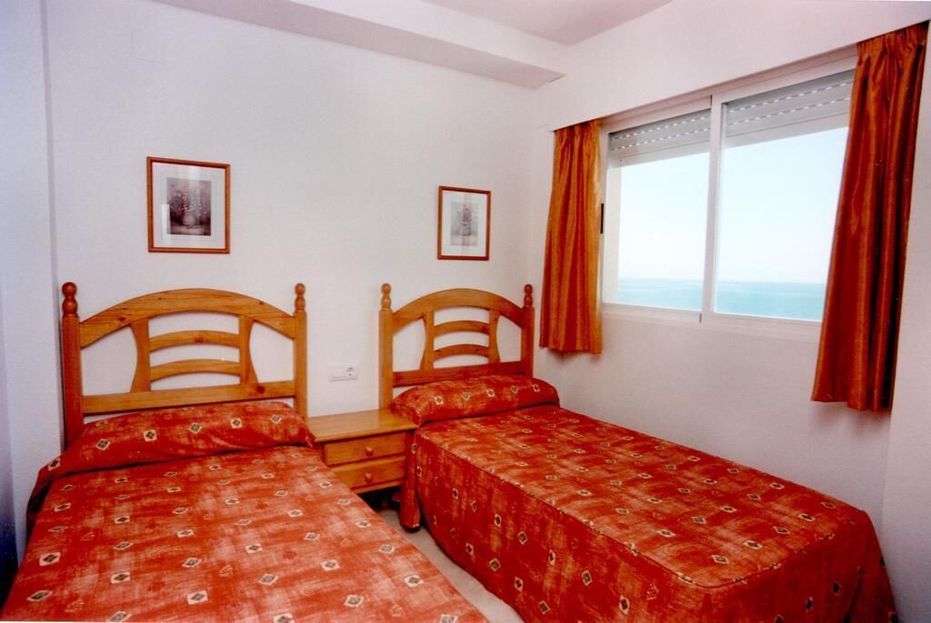 A room with two wooden beds, a small bedside table, and a window with curtains.
