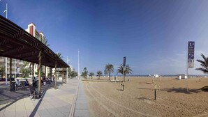 A beachside promenade with a covered walkway, palm trees, and a sandy beach. - Biarritz Apartments (Gandia)