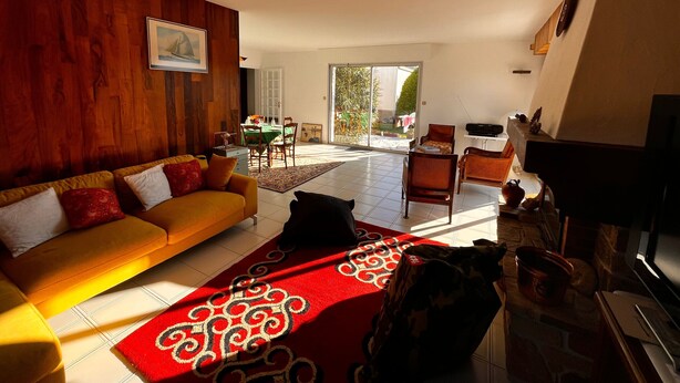 Una sala de estar amplia con un sofá amarillo, un tapete rojo con estampado y un comedor con mesa y sillas.