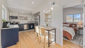 A modern kitchen with a central island, a dining area with a table and chairs, and a bedroom with a bed and window. - Tennyson Boho Stay • Fenced Yard • Pet-Friendly (Denver)