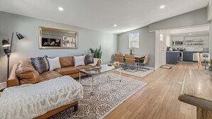 A modern living room with a leather sofa, a glass coffee table, and a dining area with a table and chairs. - Tennyson Boho Stay • Fenced Yard • Pet-Friendly (Denver)
