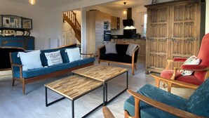A spacious living room with a sofa, armchairs, and a coffee table. A kitchen is visible in the background. - Charming House with Garden, WiFi in Central Perros-Guirec - Near Beach and Shops (Perros-Guirec)