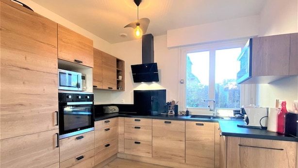 A modern kitchen with wooden cabinets, a built-in oven, and a large window providing natural light. - Charming House with Garden, WiFi in Central Perros-Guirec - Near Beach and Shops (Perros-Guirec)