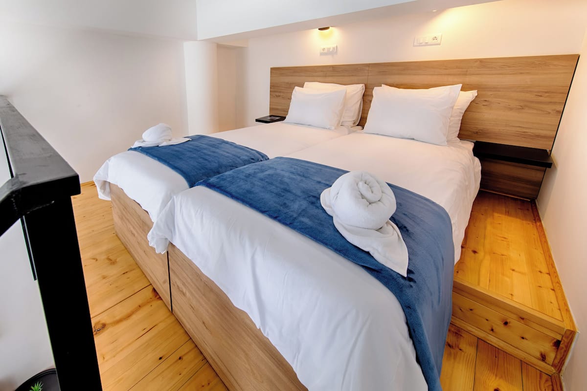 A double bed with white and blue bedding, wooden headboard, and a bedside table.