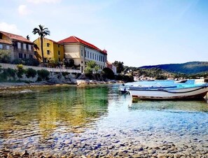 A river with boats, a stone path, and buildings along the riverbank. - 1901-on-sea (Vis)
