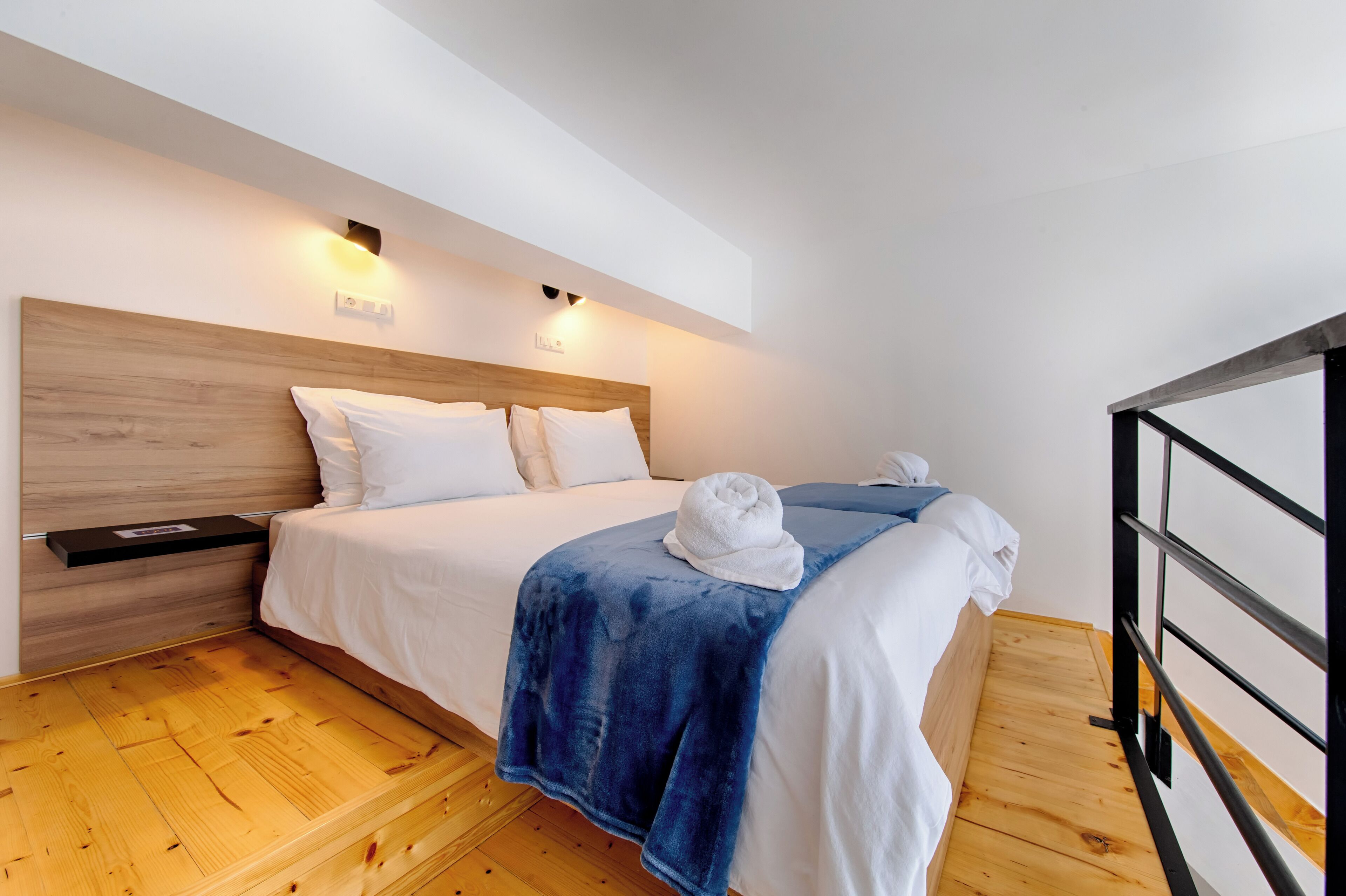 Un dormitorio con cabecera de madera, cama con ropa blanca, una manta azul y una toalla sobre la cama.