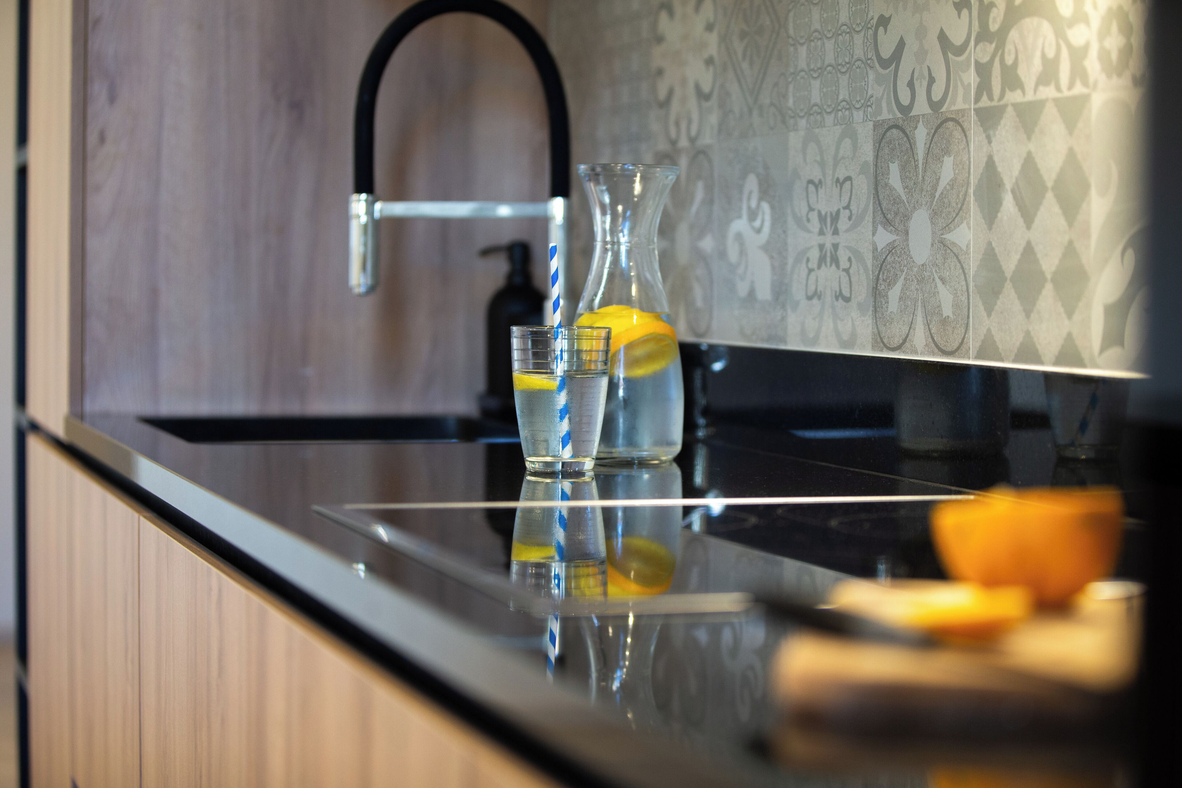 Een keuken met een modern ontwerp, met een zwart aanrecht, een roestvrijstalen spoelbak en een decoratieve achterwand.