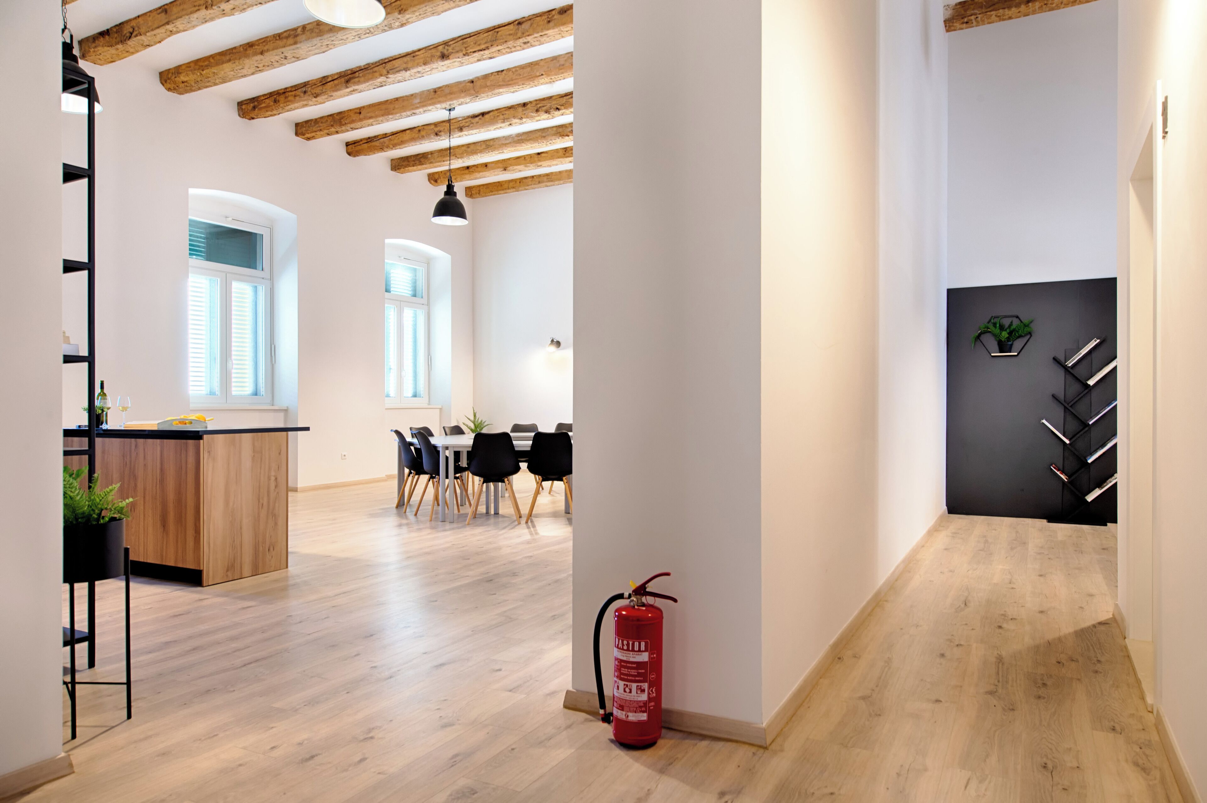 A modern interior with exposed wooden beams, a dining area with black chairs, and a fire extinguisher near the wall.
