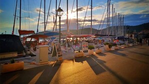 A marina with multiple sailboats docked, a covered area with seating, and a sign indicating a car rental service. - 1901-on-sea (Vis)