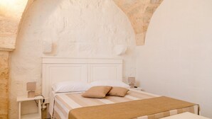 A bedroom with a stone archway, a white bed with a striped blanket, and bedside lamps. - Holiday home in the countryside with private beach in Punta Prosciutto (Manduria)