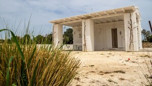 A white building with a covered patio area, surrounded by tall grasses and a clear sky. - Holiday home in the countryside with private beach in Punta Prosciutto (Manduria)