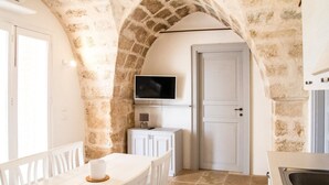 A kitchen with a stone archway, white cabinets, a TV mounted above the counter, and a sink. - Holiday home in the countryside with private beach in Punta Prosciutto (Manduria)