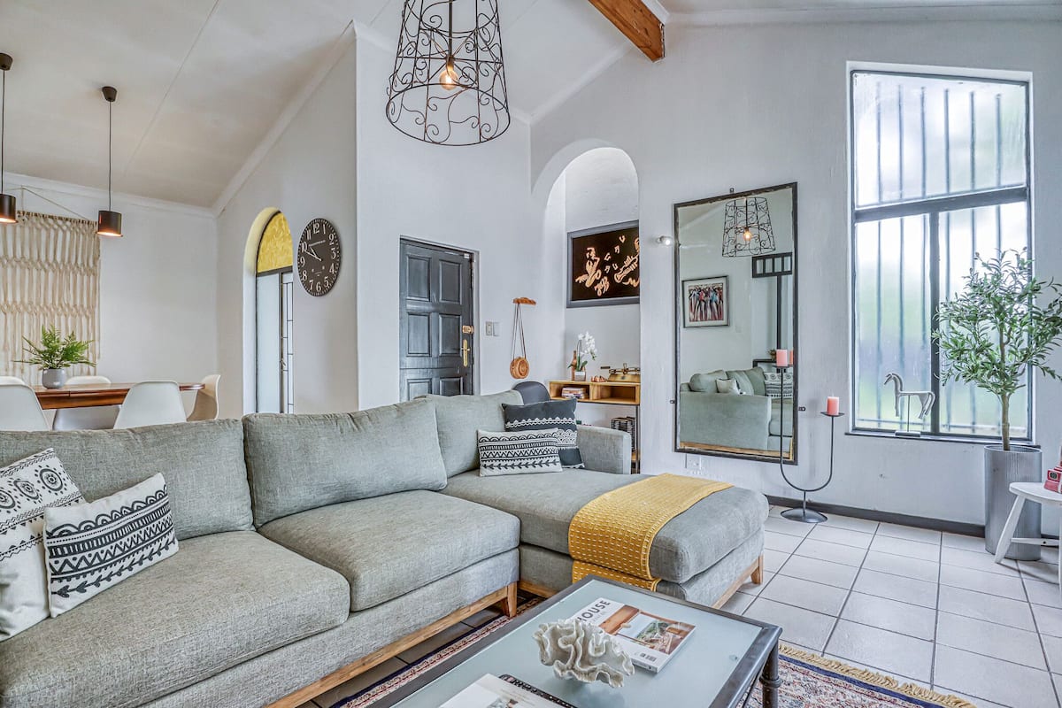 Una sala de estar moderna con un sofá seccional gris, una mesa de centro, un área de comedor con una mesa y sillas, y un ventanal con vistas.