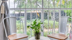 A room with a large window, two white metal chairs, a small round table, and a potted plant. - Spanish House (Centurion)