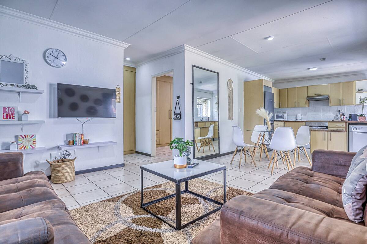Una sala moderna con sofá, una mesa de centro y televisor. Incluye una zona de cocina con alacenas y microondas.