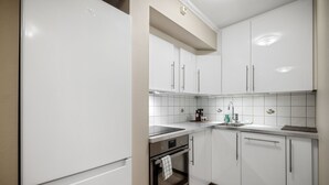 A modern kitchen with white cabinets, a stainless steel refrigerator, a built-in oven, and a sink with a faucet. - Holmboe Apartment  (Bergen)