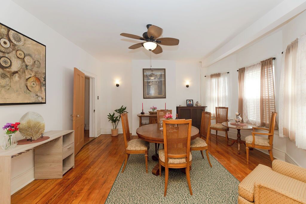 Un comedor con una mesa redonda, seis sillas, un ventilador de techo y un cuadro en la pared.