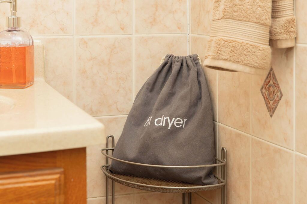 Un baño con un perchero que sostiene una bolsa gris para toallas con la etiqueta 'secadora' y una botella de jabón líquido naranja sobre el mostrador.