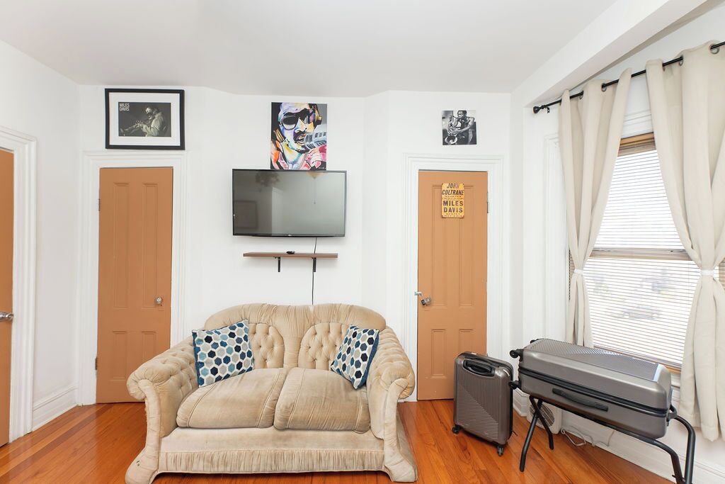 A room with a beige sofa, a flat-screen TV, a suitcase, and a sign on the door.