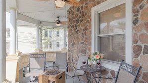 A covered patio with stone walls, a table with chairs, and a small wooden table. - The Jewel: Spacious 3 Bdrm Victorian Apt w/ Sauna, Parking. Just 10 mins To NYC! (Jersey City)