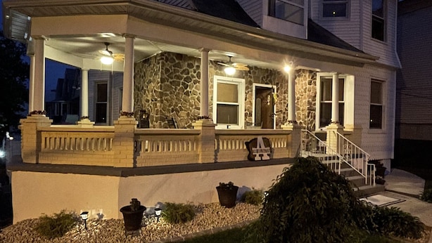 A two-story house with a stone facade, a covered porch, and a staircase leading to the second floor. - The Jewel: Spacious 3 Bdrm Victorian Apt w/ Sauna, Parking. Just 10 mins To NYC! (Jersey City)
