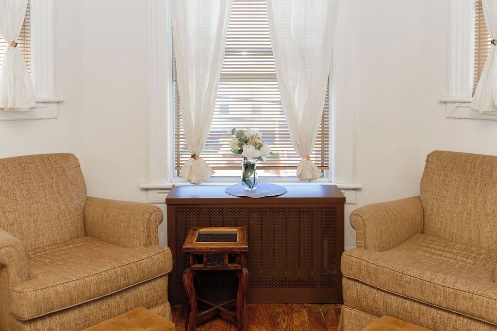 A room with two beige sofas, a small wooden table, and a vase with flowers on a windowsill.