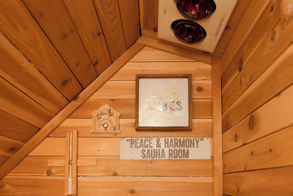 A wooden sauna room labeled "Peace & Harmony" with a thermometer, a framed sign, and a decorative house-shaped object.