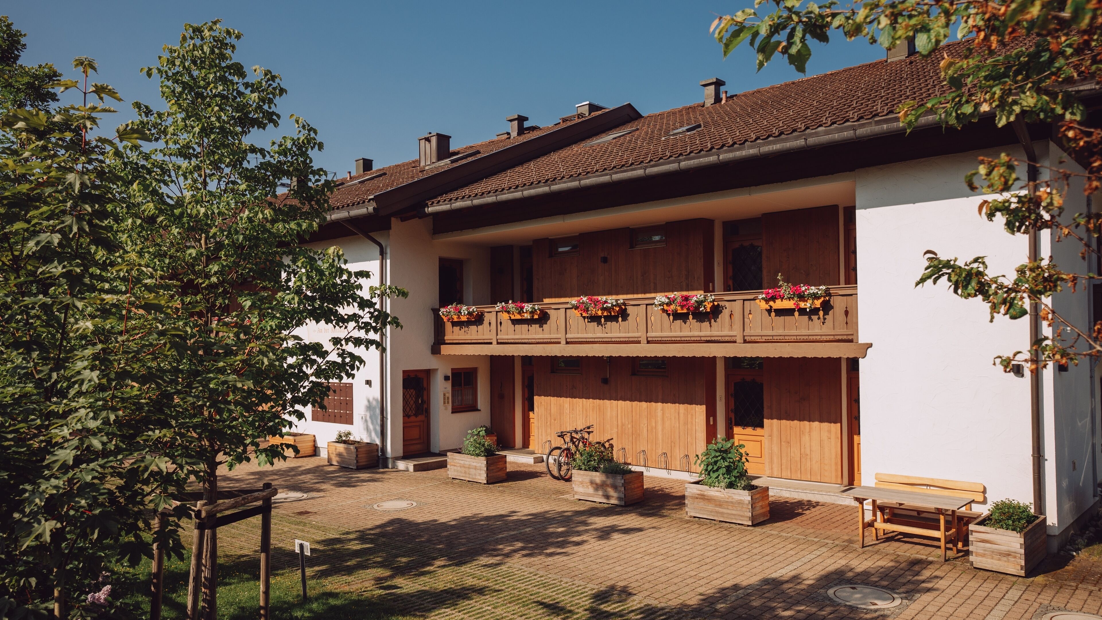 Ein zweistöckiges Holzhaus mit einem Balkon, der mit Blumen, einer Holzbank und Topfpflanzen geschmückt ist.