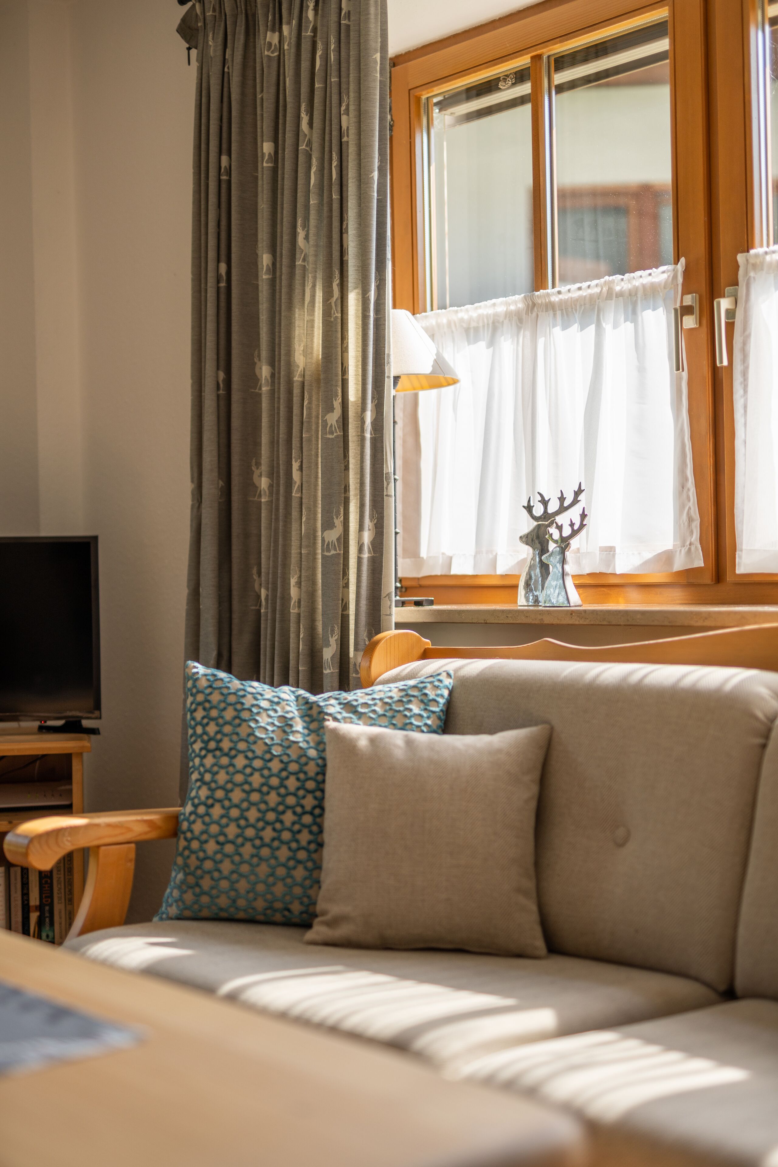 A living room with a sofa, a television, a window with curtains, and a decorative deer figurine.