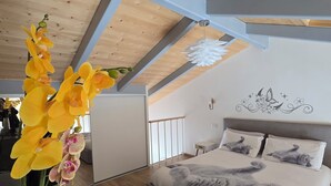 A bedroom with a sloped ceiling, a bed with a gray blanket, and a vase with yellow flowers. - BRAND NEW APARTMENT JUST MINUTES FROM THE SEA (Sarzana)