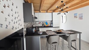 A modern kitchen with wooden beams, a dining area with chairs, and a kitchen island. - BRAND NEW APARTMENT JUST MINUTES FROM THE SEA (Sarzana)