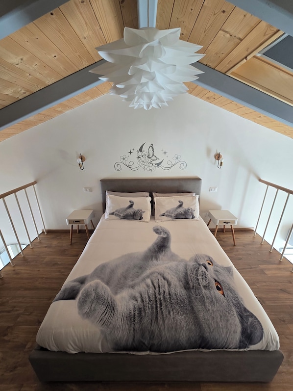 A bedroom with a wooden ceiling, a bed with a cat, and a decorative wall.