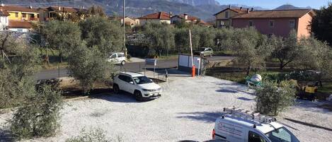 A parking area with several cars, a white van, and a yellow vehicle. There are buildings in the background with a mountainous landscape.