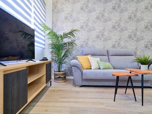 Un salon moderne avec un canapé gris, une table basse en bois et un téléviseur posé sur un meuble en bois.