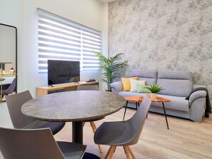 Ein modernes Wohnzimmer mit rundem Tisch, grauem Sofa und großem Fernseher.