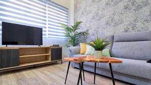 Una sala moderna con televisor de pantalla plana, mueble de entretenimiento de madera, sofá gris y una mesita con planta en maceta.
