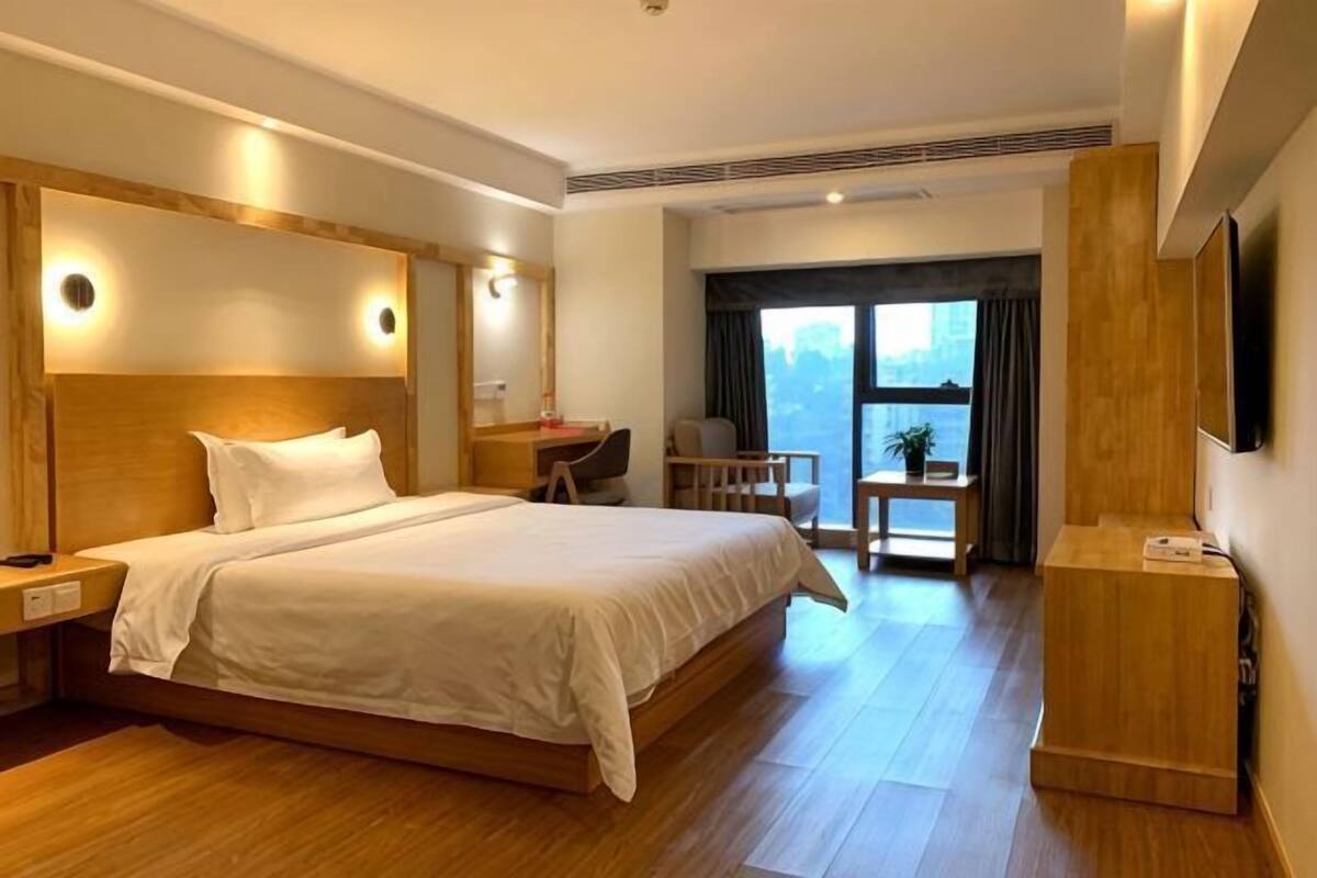 A hotel room with a large bed, a desk, a chair, a TV, and a view of the city.