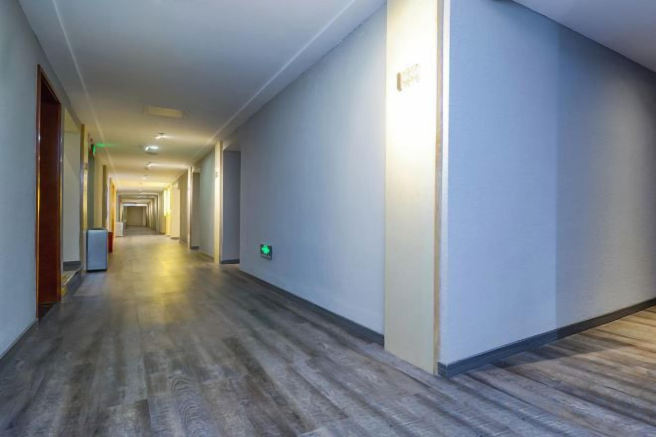 A long, narrow hallway with a wooden floor and white walls, leading to a door at the end.
